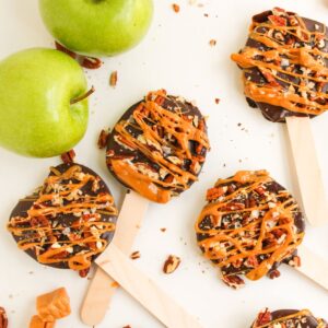Apple slices on wooden sticks with a chocolate coating drizzled with caramel and pecans.
