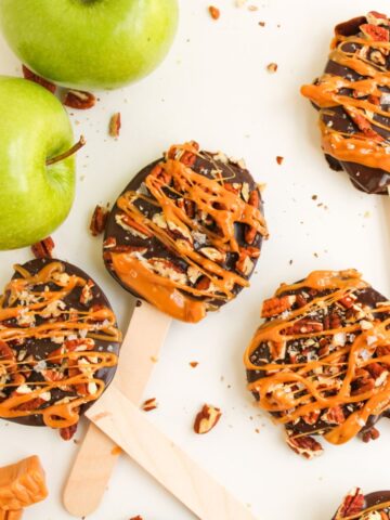 Apple slices on wooden sticks with a chocolate coating drizzled with caramel and pecans.