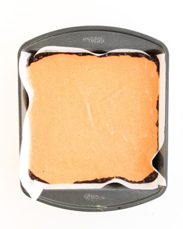 A square baking pan with a base layer of brownies topped with a creamy pumpkin layer to make pumpkin spice brownies with a cream cheese swirl