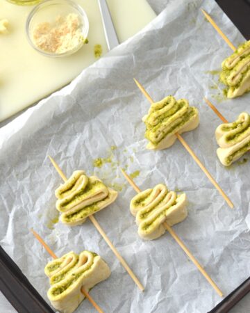 Crescent dough with a basil pesto filling shaped into Christmas trees with wooden skewers though the center.