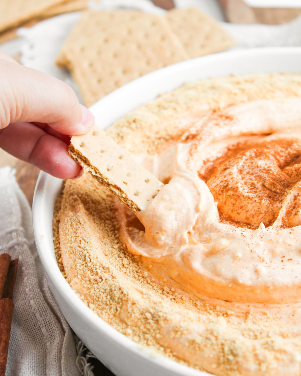 A ceramic bowl with a creamy pumpkin dip that is no bake in the bowl.A graham cracker is being dipped into the bowl.