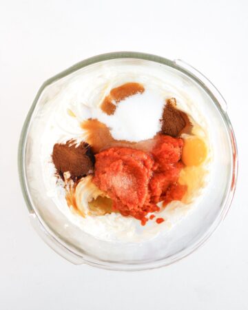 A glass mixing bowl with whipped cream cheese, spices, and pumpkin puree to make a cream cheese pumpkin swirl for pumpkin brownies with a cream cheese swirl.