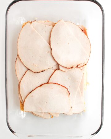 A glass baking dish with a layer of slider rolls topped with leftover turkey to make cranberry turkey sliders.