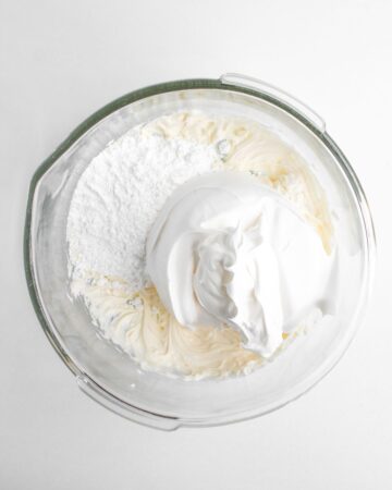 A glass mixing bowl with cream cheese and confectioners sugar being mixed. 