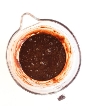 A glass measuring cup with brownie mix and pieces of dark chocolate to make the base of pumpkin spice brownies.