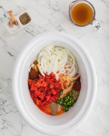 A white slow cooker vessel with sliced onions, tomatoes,