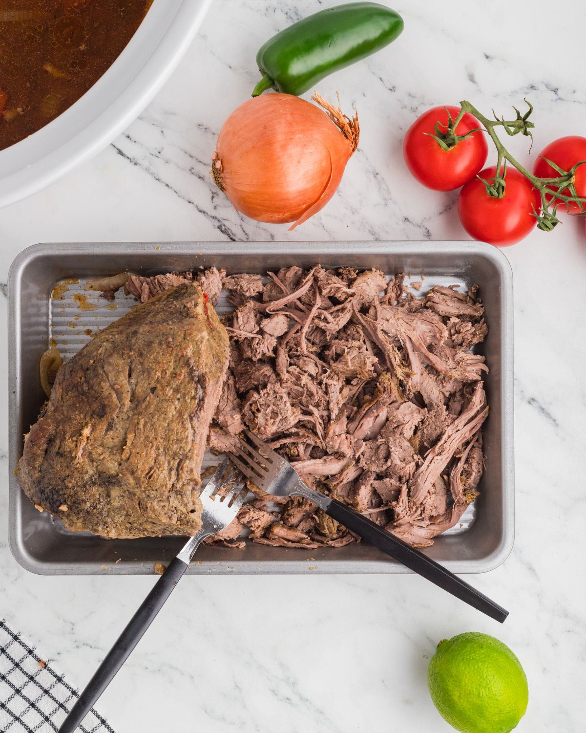 Shredded beef, Mexican style in a silver tray with onions, jalapenos, and tomatoes around the beef.
