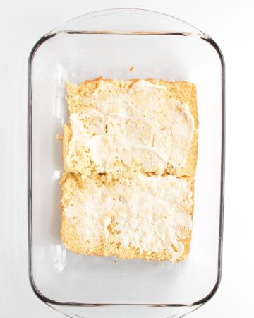 A glass baking dish with tghe bottom of hawaiian rolls topped with mayonnaise in the casserole dish.