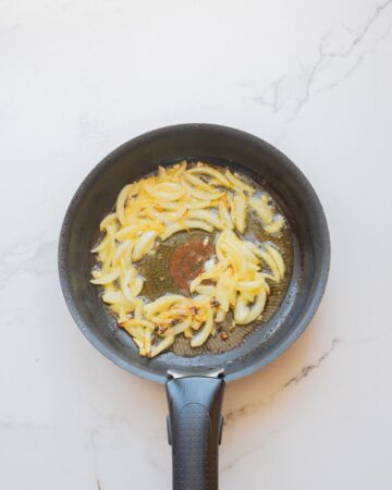 An oven safe skillet with sauteed onions for butter chicken.