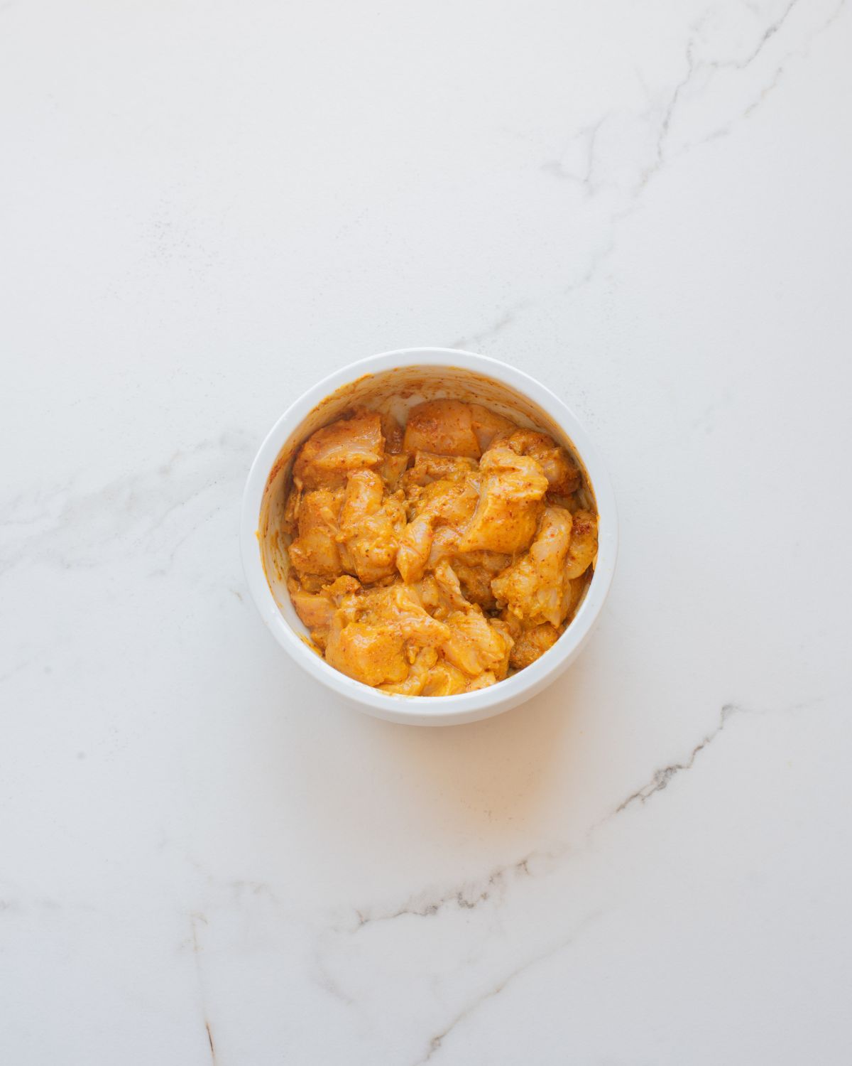 A white bowl with boneless chicken thighs in a butter chicken marinade with yogurt and spices.