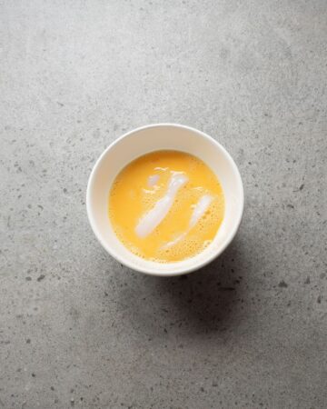 A white bowl with an egg wash with raw calamari ring in the egg wash.