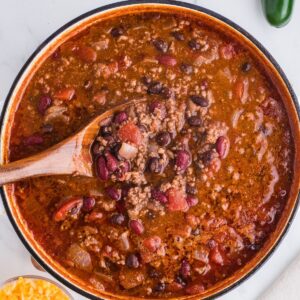 Smoky Chipotle Chili in a brown ceramic bowl and a wooden spoon picking up a scoop of chili.