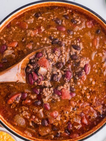 Smoky Chipotle Chili in a brown ceramic bowl and a wooden spoon picking up a scoop of chili.