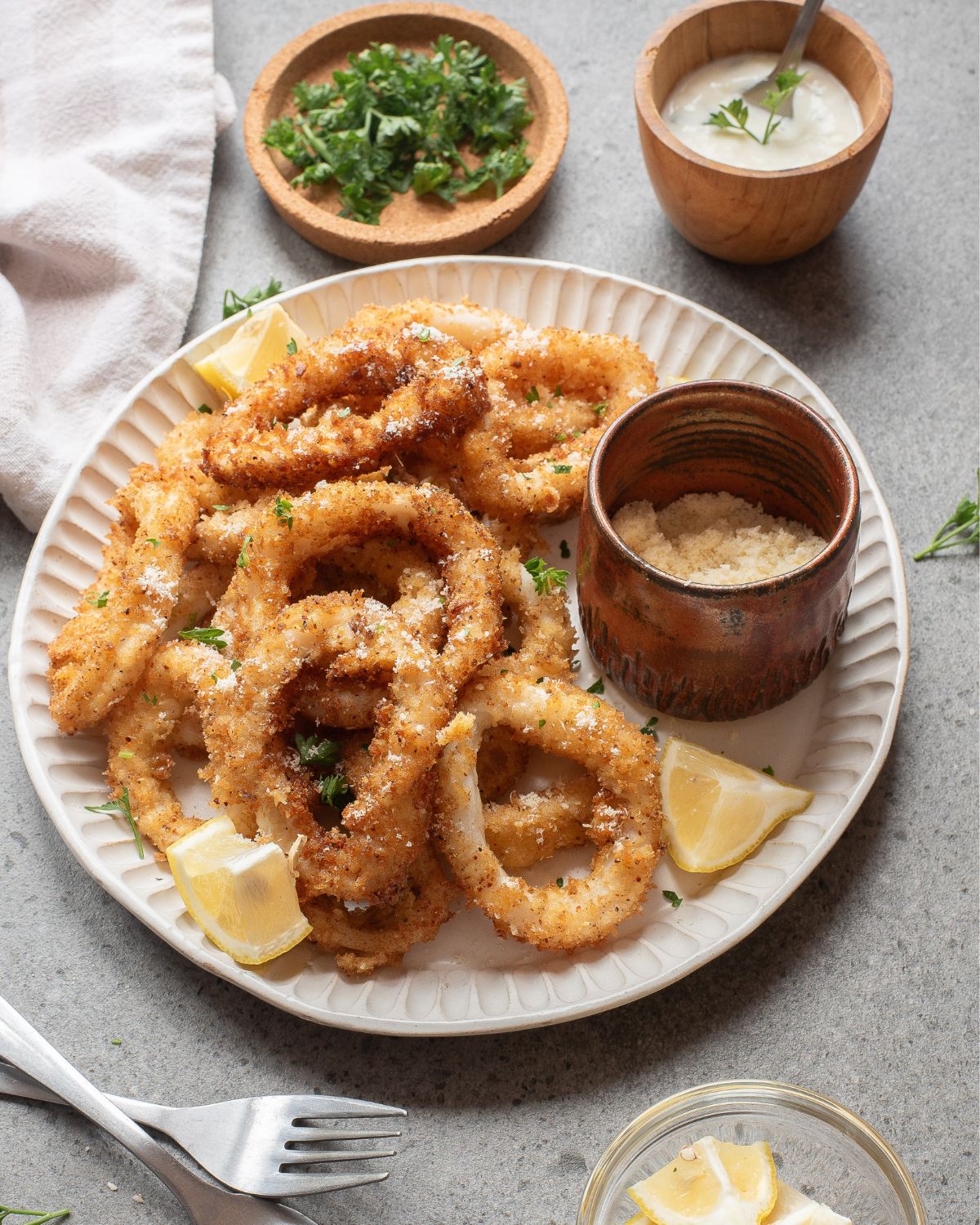 A white ceramic bowl with baked breaded calamari and a silver bowl of aioli on the side.