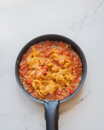 An oven safe saute pan with chicken thighs in an Indian butter sauce.