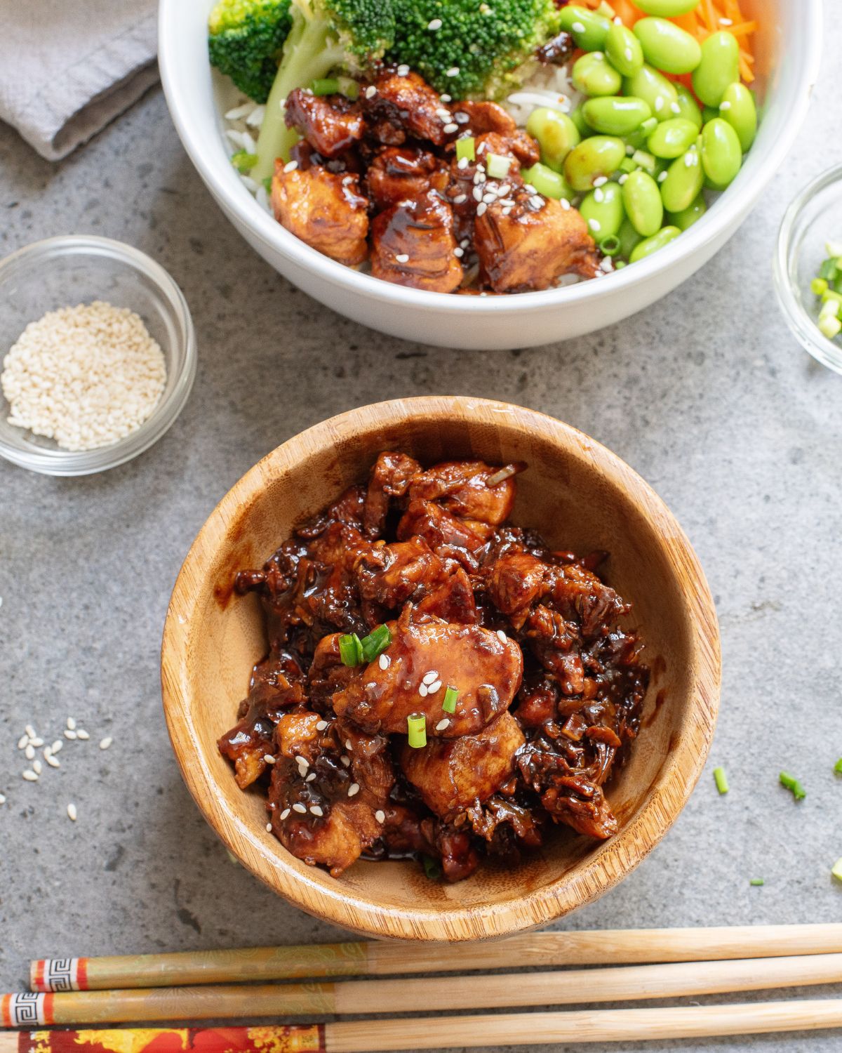 Teriyaki chicken in a brown bowl and wooden chopsticks and a white bowl with teriyaki chicken and rice bowls.