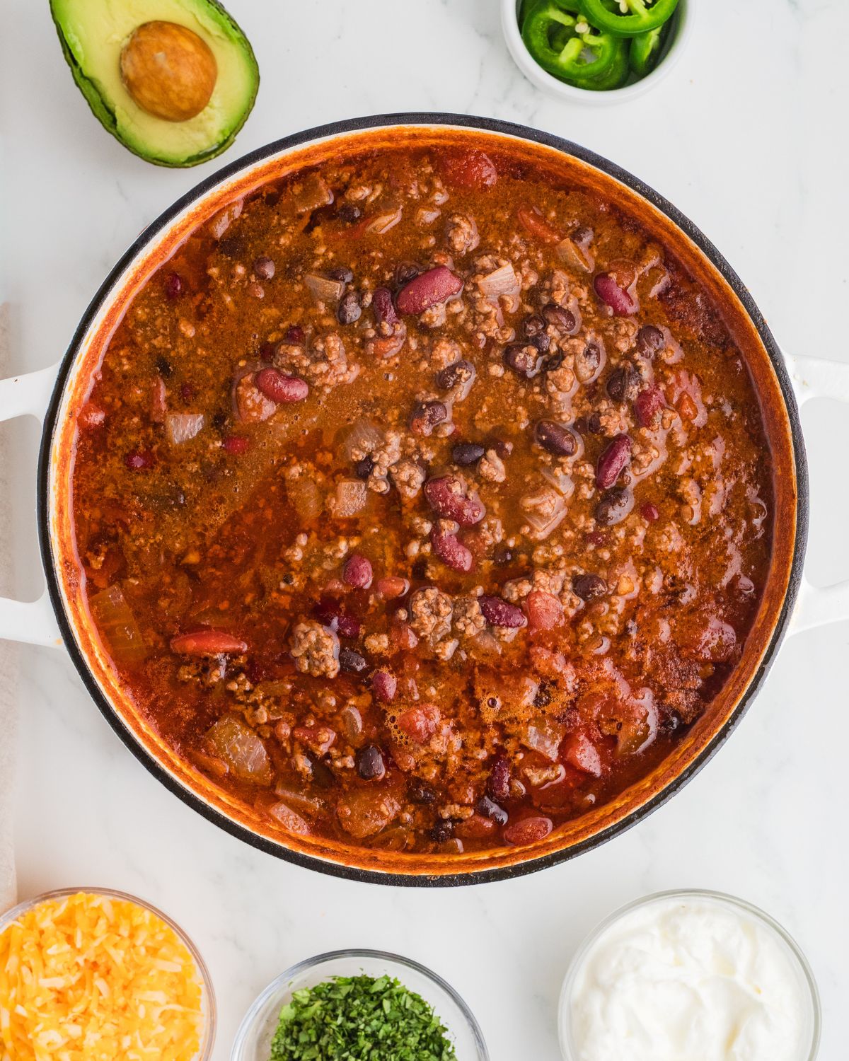 A dutch oven filled with chipotle chili with ground beef, beans, diced tomatoes, and crushed tomatoes with chipotle chilis in adobo sauce.