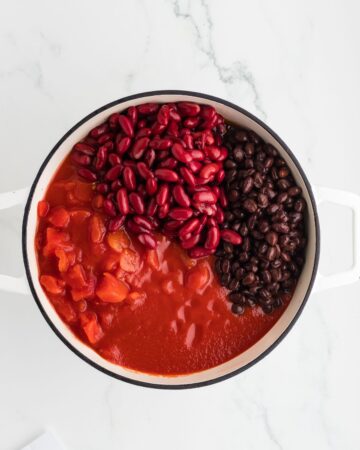 A dutch oven with kidney and black beans, diced tomatoes, and crushed tomatoes for a Chipotle Chili recipe.