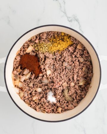 A white Dutch Oven with browned ground beef and spiced for the base of Chipotle Chili.