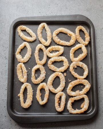 A baking tray with breaded calamari rings ready to be baked in the oven.