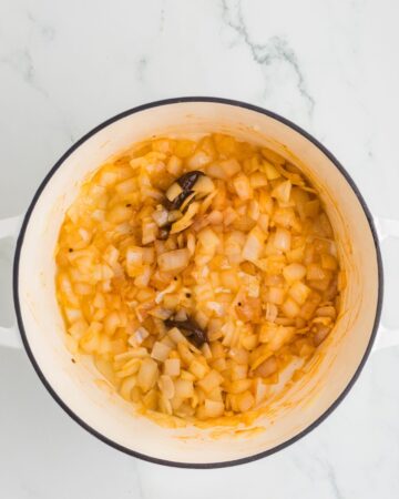 A white Dutch Oven with sauteed onion and chipotle peppers in adobo to make Chil with ground beef and chipotle peppers.
