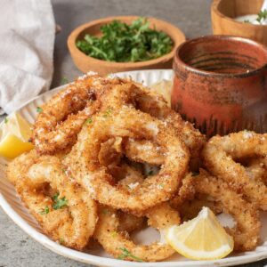 A plate of baked calamari with a panko breading and a lemon wedge on the side.