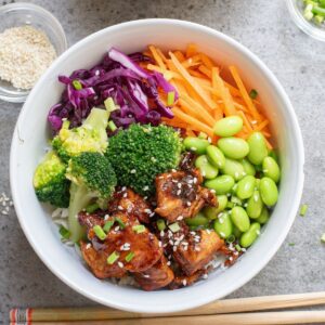 teriyaki chicken and rice bowl with veggies in a white bowl.