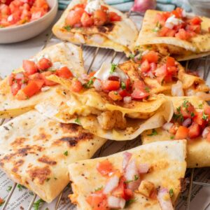 Triangles of shrimp quesadillas topped with a pico de gallo on a wire rack.