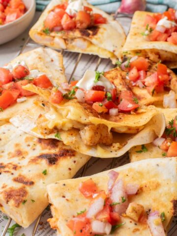 Triangles of shrimp quesadillas topped with a pico de gallo on a wire rack.