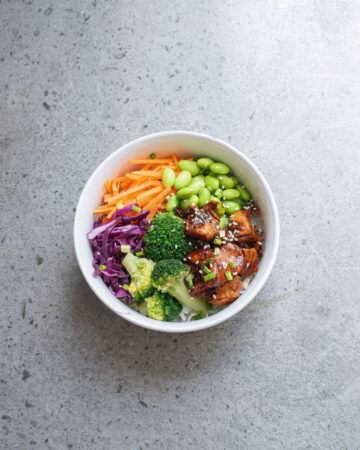 A white bowl with teriyaki chicken and vegetables over rice to make a teriyaki chicken rice bowl.