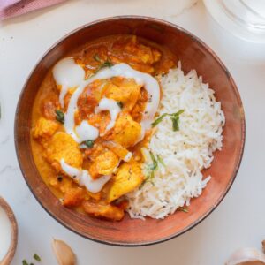 A brown bowl with butter chicken and basmati rice.