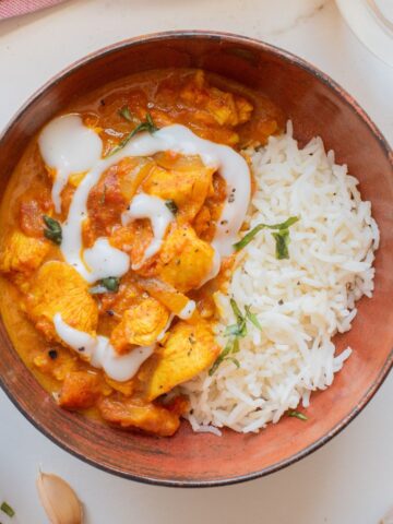 A brown bowl with butter chicken and basmati rice.