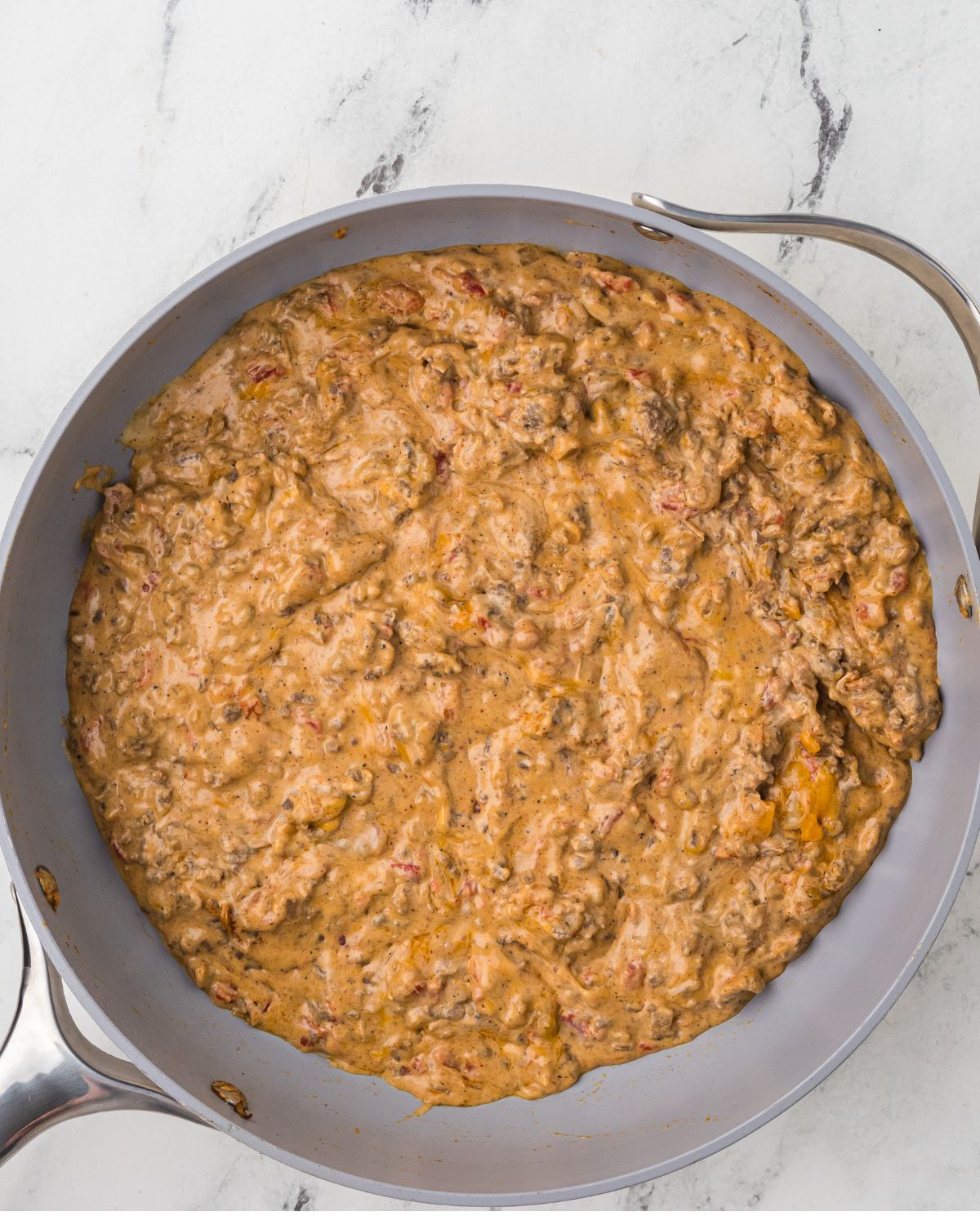 A saute pan with ground beef and cheese to make a chili cheese dip.