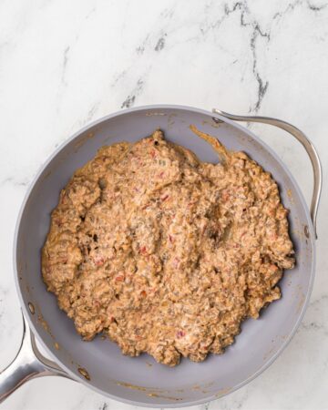 A saute pan with ground beef, diced tomatoes, spices, and cream cheese mixed together for the base of chili cheese dip.