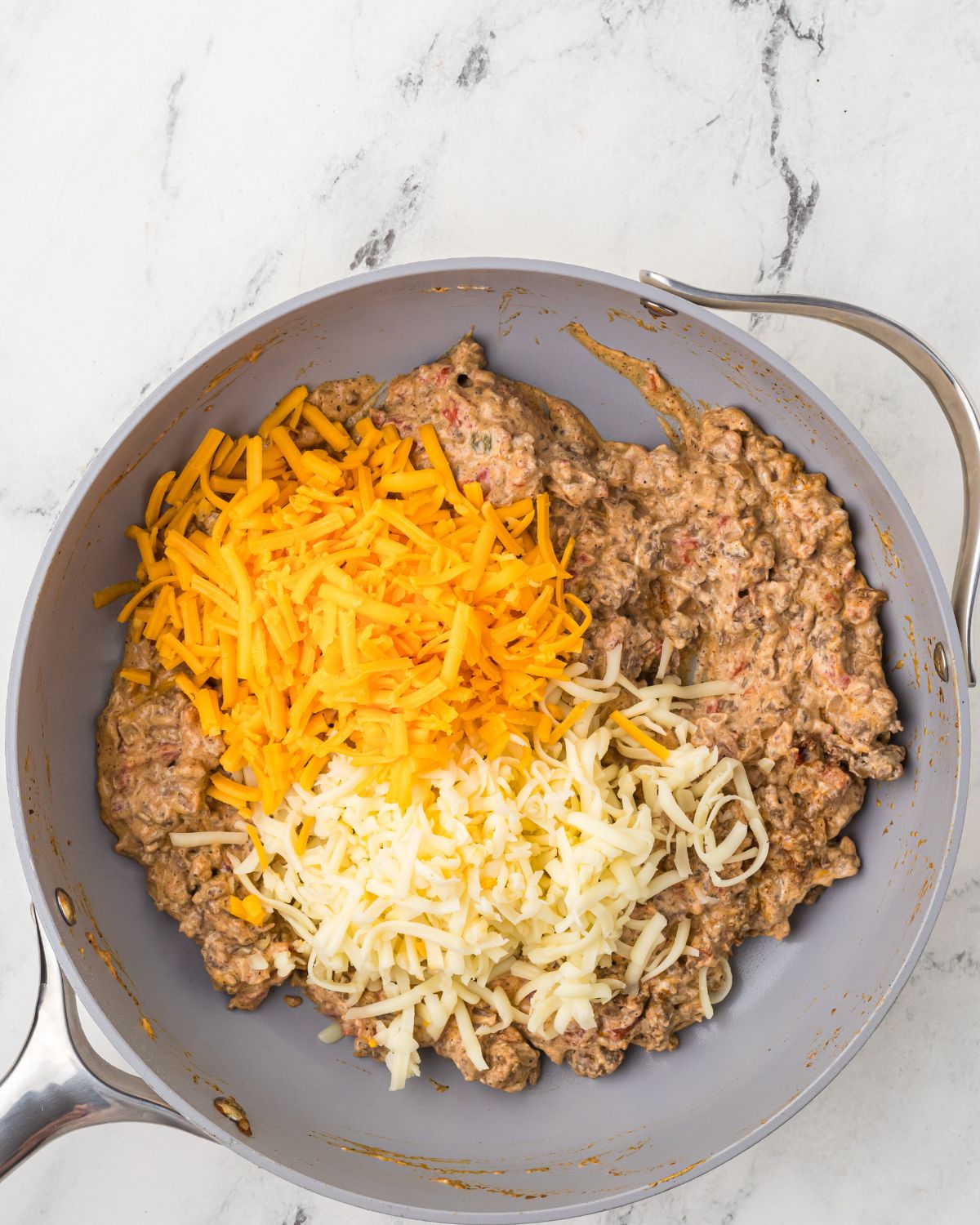 A saute pan with the ground beef and adding cheddar cheese and Monterey jack cheese to make chili cheese dip recipe.