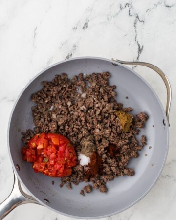 Ground beef, diced tomatoes and spices in a saute pan to make chili cheese dip recipe.