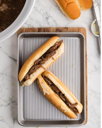 A silver tray with french dip sandwiches made in the slow cooker with provolone cheese.
