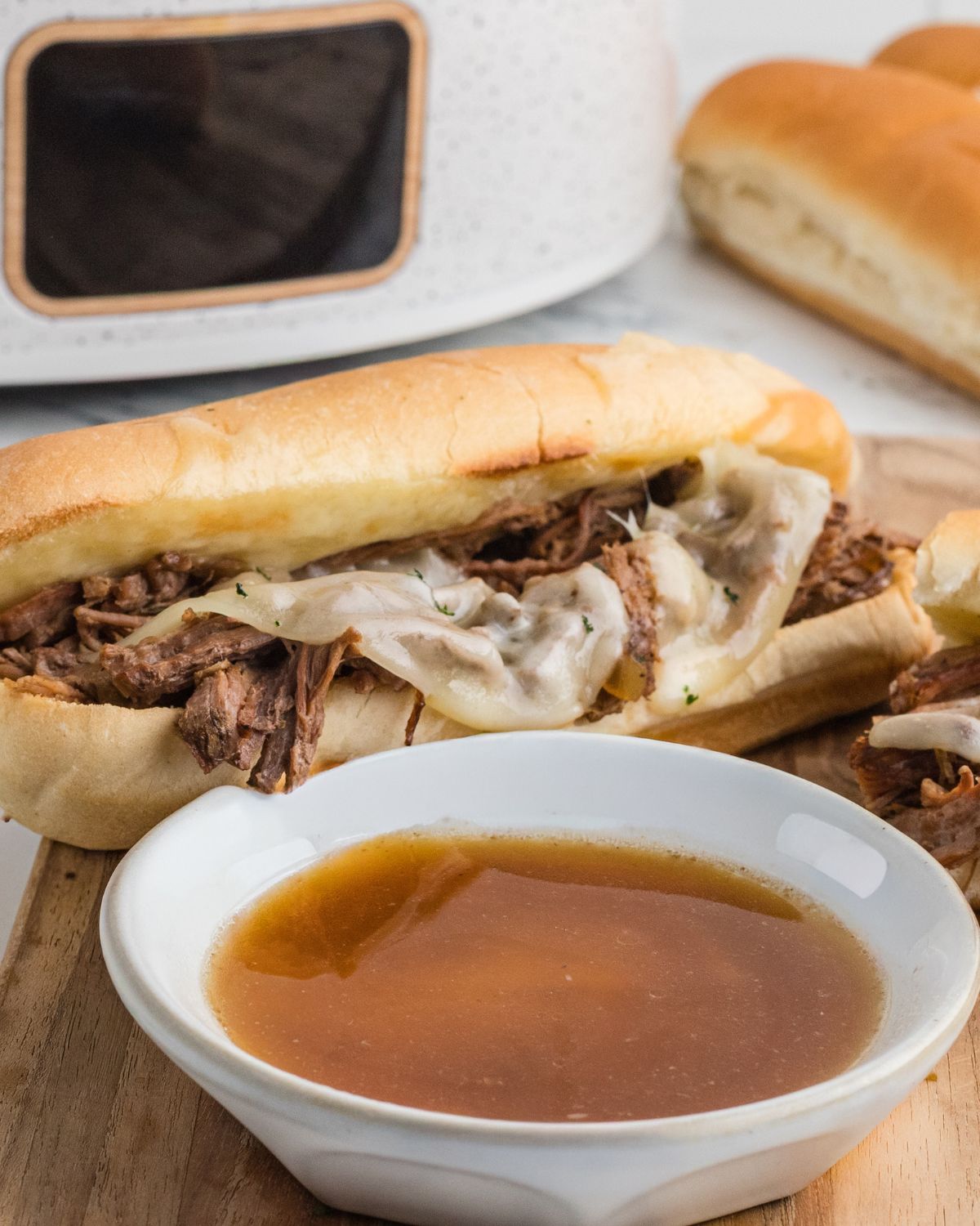 A wooden cutting board with hoagie rolls with slow cooker beef dip french sandwiches with provolone cheese 