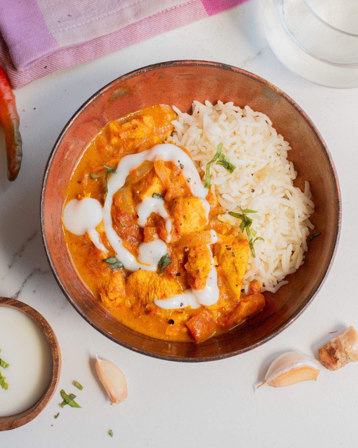 A wooden bowl with basmati rice and butter chicken topped with a drizzle of yogurt and chopped cilantro.