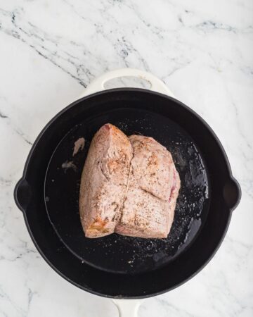 A cast iron pan a a roast being seared to make Crockpot French Dip Sandwiches.