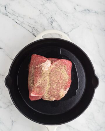 A cast iron pan with a seasoned rump roast to sear for a slow cooker french dip sandwich.
