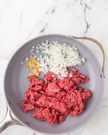A saute pan with ground beef, onions, and garlic to be sauteed to make a chili cheese dip.