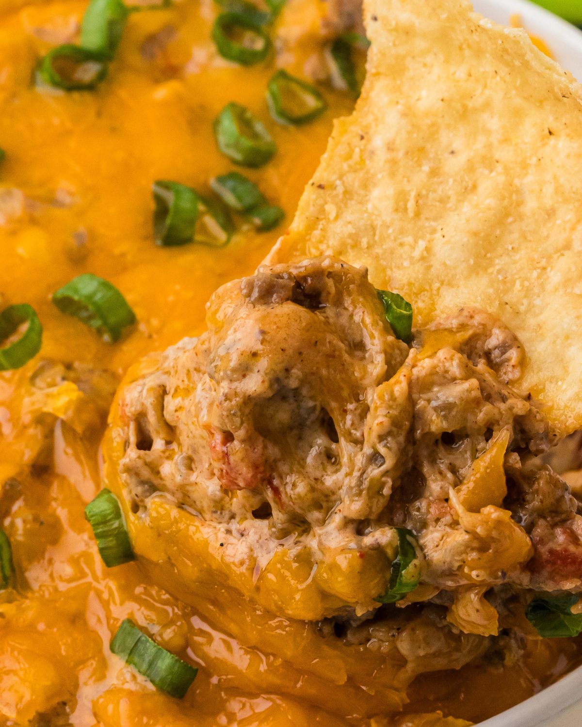 A tortilla chip being dipped into the ground beef and cheese dip.