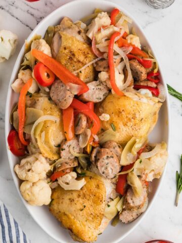 A platter of Italian American Chicken Scarpariello with cauliflower, red peppers, artichokes, sausage, and cherry peppers.