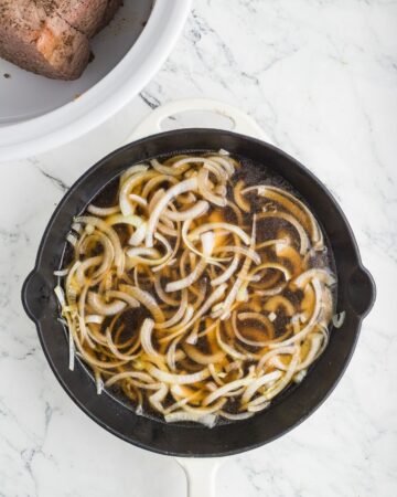 A cast iron pan with sliced onions and beef broth to begin the base of the au jus for french dip beef sandwiches. 