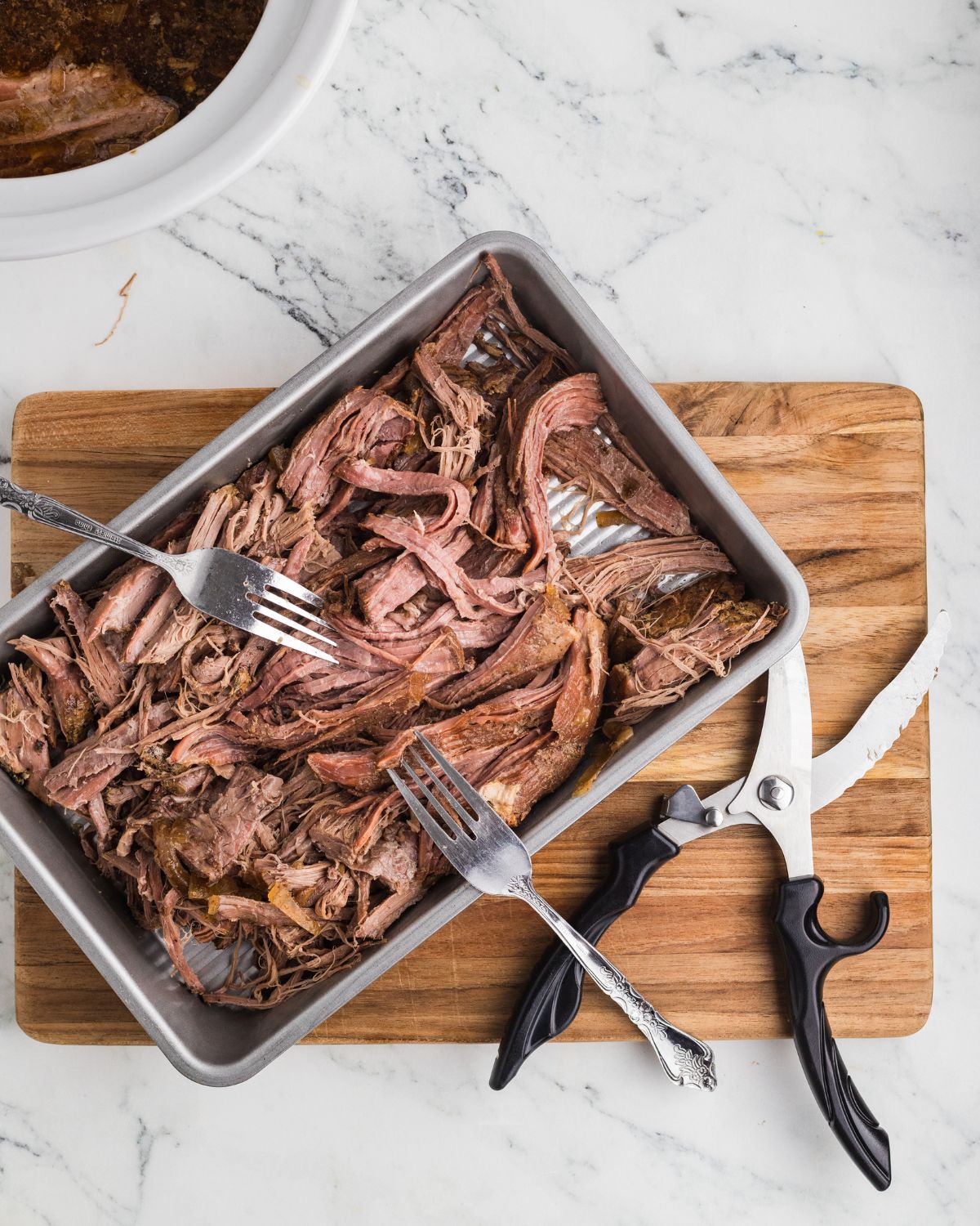 A silver tray with shredded beef french dip sandwiches in the slow cooker.