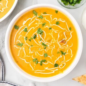 Cauliflower and sweet potato soup in a bowl with a sour cream drizzle and chopped parsley on top.