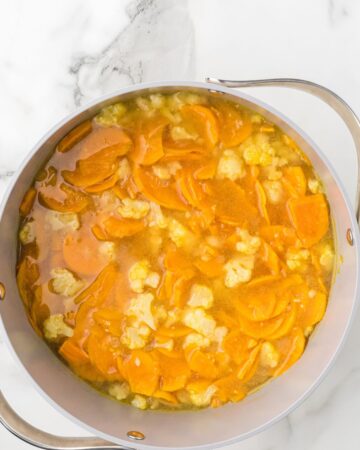 A soup pot with cauliflower florets, sweet potatoes, and chicken stock to make a sweet potato cauliflower soup.