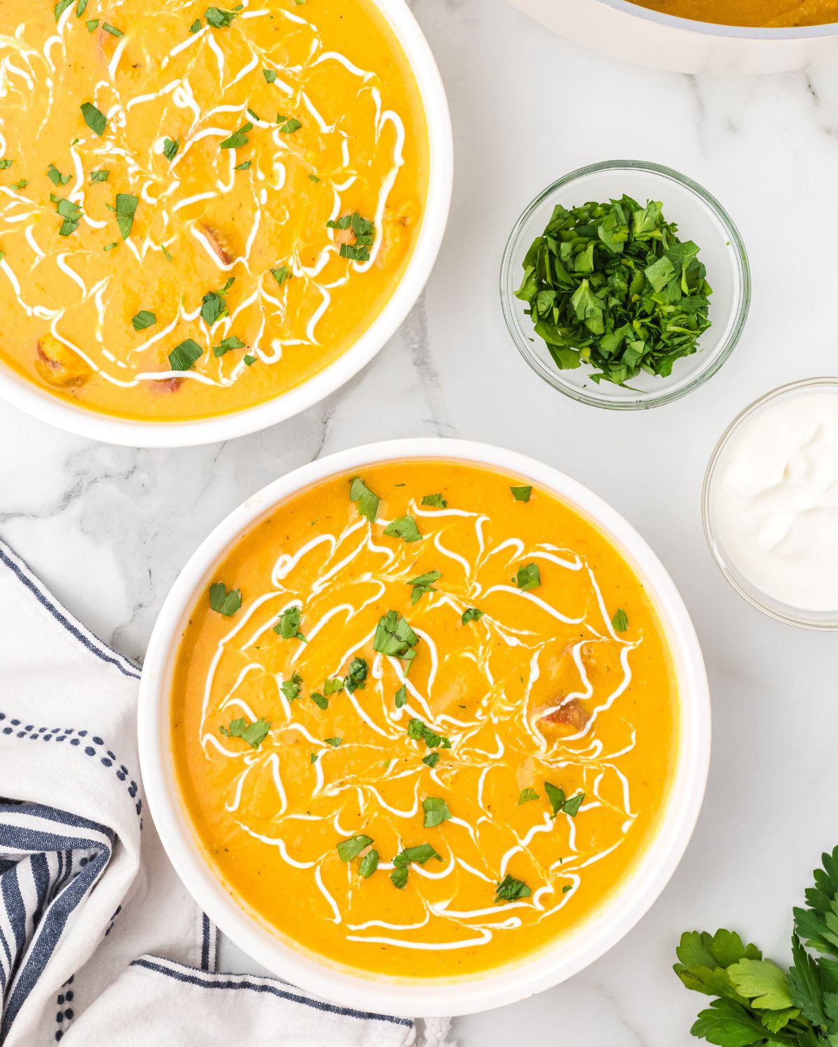 An overhead view of sweet potato cauliflower soup with a drizzle of sour cream and parsley.