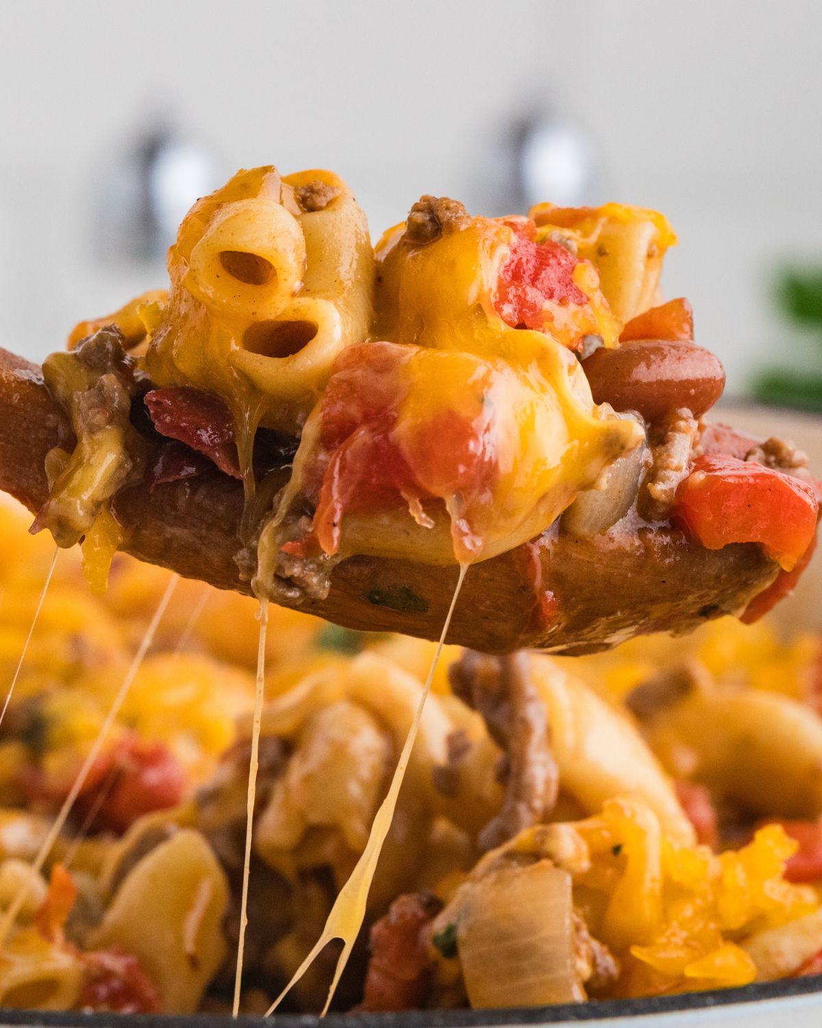 A wooden spoon with chili mac and cheese being picked up.